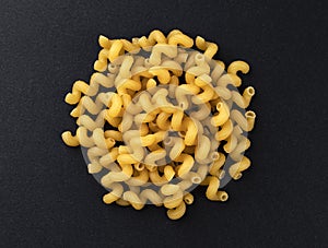 Raw cellentani pasta isolated on black background, top view