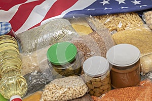 Raw cereals, jars of marinades, pasta, porridge and grains on the table, the American flag. Concept: humanitarian aid with essenti