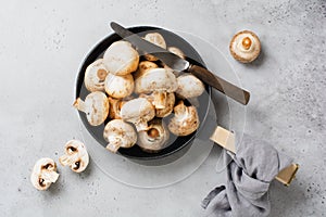 Raw Champignon mushrooms in a cast-iron old pan on an old concrete gray rustic background for frying. Top view