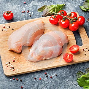 Raw chicken breast fillet with greens, tomatoes and spices on a dark background