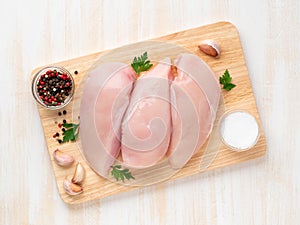 Raw chicken breast fillet with spices on wooden board on white wooden table, top view