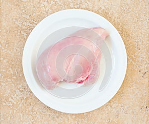 Raw chicken breast fillets on a white plate top view