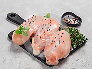 Raw chicken breast with fresh basil on black cuttingboard over cement background