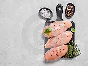Raw chicken breast with fresh basil and thyme on black cuttingboard, copyspace