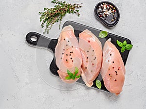 Raw chicken breast with fresh basil and thyme on black cuttingboard, copyspace