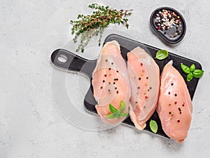 Raw chicken breast with fresh basil and thyme on black cuttingboard, copyspace