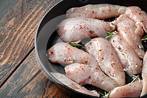 Raw chicken breast mini fillets in rastic cast iron skillet, frying pan with herbs and sea salt photo