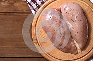 Raw chicken breast sprinkled with black pepper and salt lies on a round wooden Board