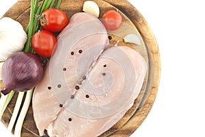 Raw chicken breasts on wooden cutting board with vegetable, isolated on white background. Top view