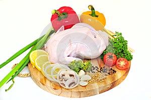 Raw chicken on a cutting board with garnished vegetables with a white background