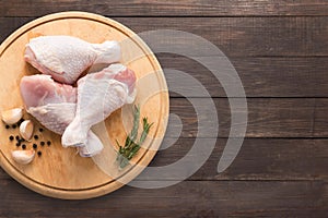 Raw chicken drumsticks on cutting board on wooden background.