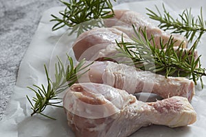 Raw chicken drumsticks with rosemary on greaseproof paper.