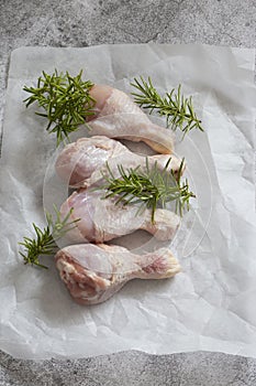 Raw chicken drumsticks with rosemary on greaseproof paper. photo
