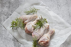 Raw chicken drumsticks with rosemary on greaseproof paper. photo