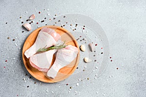 Raw chicken drumsticks with seasonings and spices on wooden plate over gray concrete table background