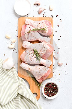 Raw chicken drumsticks with seasonings on wooden cutting board over white concrete table background with copy space