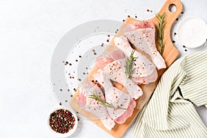 Raw chicken drumsticks with seasonings on wooden cutting board over white concrete table background with copy space