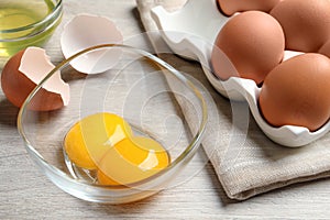 Raw chicken eggs and bowl with yolks on white wooden table