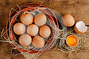 Raw chicken eggs and broken egg shell with yolk on wooden background