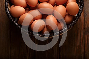 Raw chicken eggs in wicker basket on wooden table, top view. Space for text