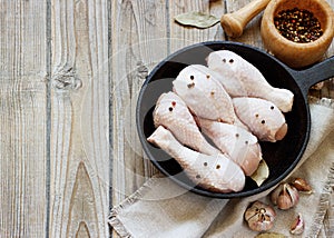 Raw chicken legs in a cast iron skillet with seasonings for cooking