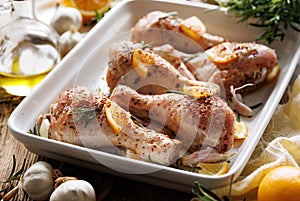 Raw chicken legs drumsticks with rosemary, garlic and lemon in a ceramic baking dish