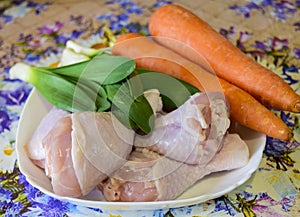 Raw chicken legs with green onions and carrots.