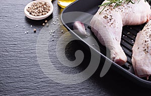 Raw chicken legs with herbs, garlic and tomatoes, ready to cook on a black stone background