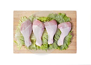 Raw chicken legs and lettuce leaf on wooden cutting board isolated on white background. Four fresh legs for cooking. Top view.
