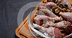 Raw chicken legs and lots of spice in a transparent dish on a dark background.