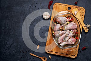 Raw chicken legs and lots of spice in a transparent dish on a dark background.