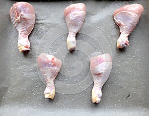 Raw chicken legs prepared for cooking in the oven on the baking pan and backing paper with salt