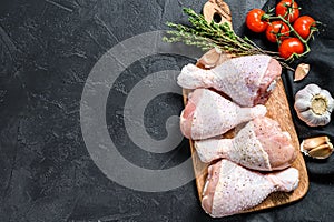 Raw chicken legs with spices and vegetables on a wooden cutting board. Black background. Top view. Copy space