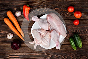 Raw chicken meat on dark wooden background with vegetables