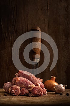 raw chicken necks with onions, garlic and peppercorns on a cutting board on a shabby wooden background. artistic vertical moody