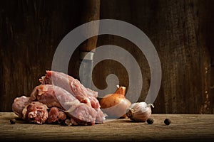 raw chicken necks with onions, garlic and peppercorns on a cutting board on a shabby wooden background. moody meat still life with