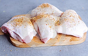 Raw chicken thigh with herbs on cutting board on grey table