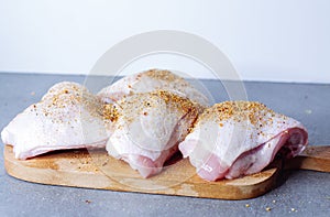 Raw chicken thigh with herbs on cutting board on grey table