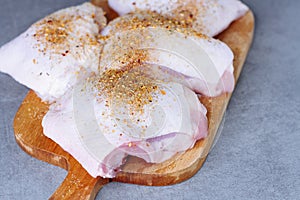 Raw chicken thigh with herbs on cutting board on grey table