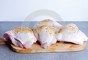 Raw chicken thigh with herbs on cutting board on grey table