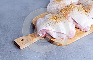 Raw chicken thigh with herbs on cutting board on grey table
