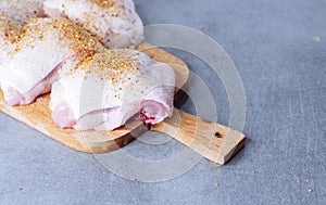 Raw chicken thigh with herbs on cutting board on grey table