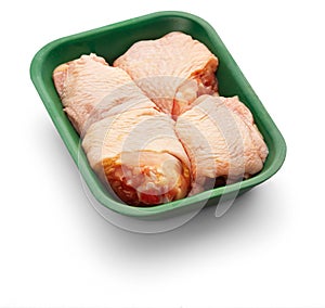 Raw chicken thighs in a green tray over white background