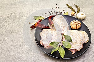 Raw chicken thighs with spices. Ingredients for cooking meat on a stone background. Hot and black pepper, garlic, rosemary, bay