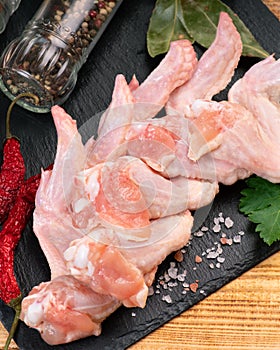 Raw chicken wings on a black kuramik kitchen board with red hot peppers and spices. Raw chicken meat.Raw chicken wings on cutting