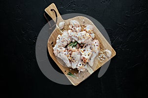 Raw chicken wings on cutting board with ingredients for cooking at black background. Fresh uncooked drumette or