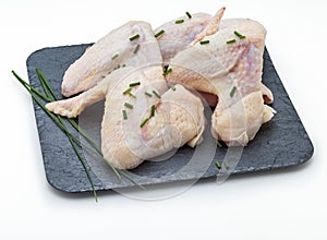 Raw chicken wings marinated with salt, pepper and chives on slate board isolated on white background