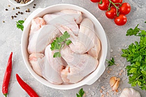 Raw chicken wings in a white dish with fresh herbs, spices for cooking on a gray concrete background. Top view, copy space