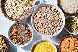 Raw chickpeas in a white bowl. Various dry cereals and legumes in white and wooden bowls, white marble background. Vegan protein