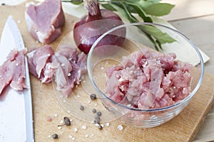 Raw chopped pork tenderloin with herbs in a glass bowl on a wooden board